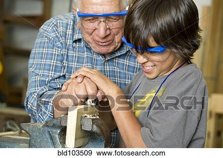 Stock Photo - Hispanic grandfather and son planing wood in workshop. Fotosearch