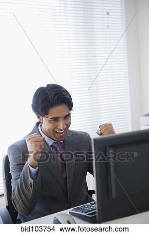 Picture - Mixed race businessman cheering at computer. Fotosearch