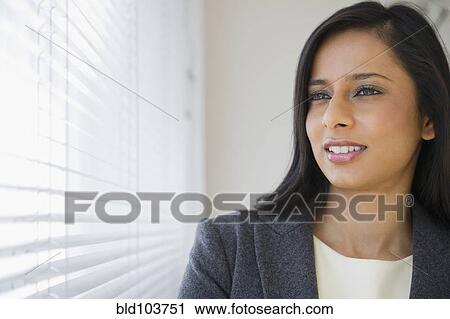 Stock Image - Mixed race businesswoman looking out window. Fotosearch