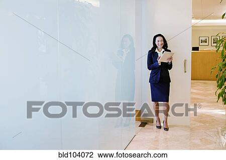 Stock Image - Mixed race businesswoman using digital tablet in office corridor. Fotosearch