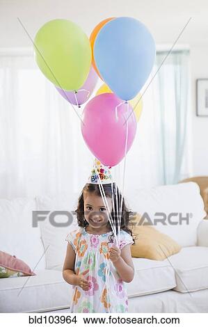 Picture - Mixed race girl in party hat holding balloons. Fotosearch