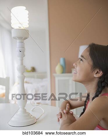 Mixed race girl looking at CFL light bulb View Large Photo Image Picture - Mixed race girl looking at CFL light bulb. Fotosearch