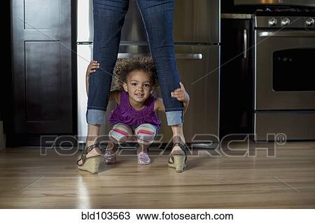 Stock Image - Mixed race girl playing underneath mother's legs. Fotosearch