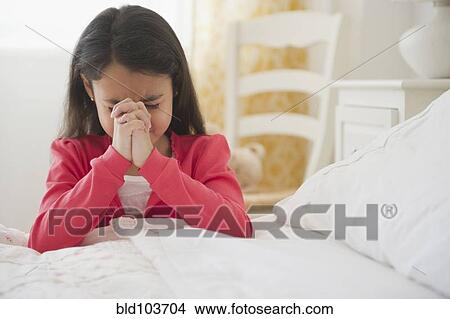 Picture - Mixed race girl praying in bedroom. Fotosearch