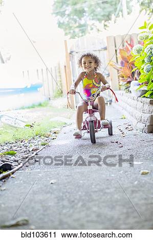 Stock Image - Mixed race girl riding tricycle. Fotosearch