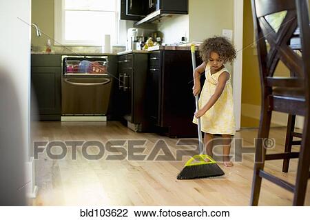 Stock Image - Mixed race girl sweeping kitchen floor. Fotosearch