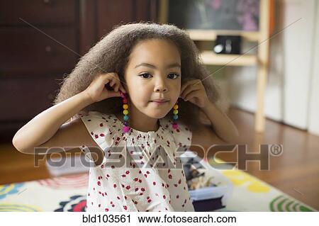 Stock Image - Mixed race girl trying on earrings. Fotosearch