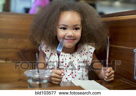 Stock Photo - Mixed race girl waiting for food in restaurant. Fotosearch