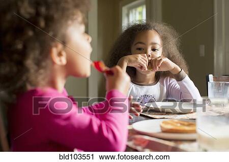 Stock Image - Mixed race girls eating breakfast. Fotosearch
