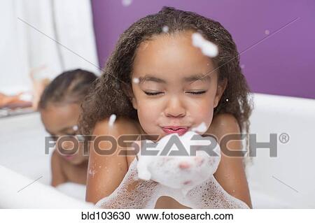 Stock Image - Mixed race girls playing with bubbles in bathtub. Fotosearch