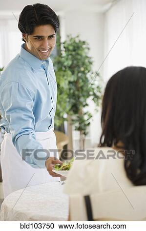 Stock Image - Mixed race waiter serving woman salad. Fotosearch