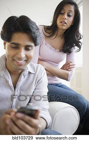 Stock Photo - Mixed race woman watching husband text messaging. Fotosearch