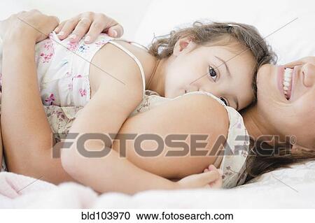 Stock Image - Mother and daughter laying on bed. Fotosearch