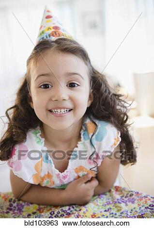 Stock Image - Smiling mixed race girl in party hat. Fotosearch