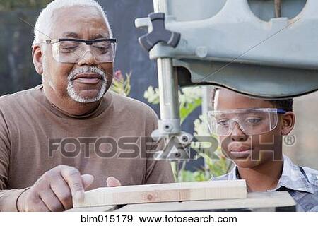 Stock Photo - African American boy watching grandfather use table saw. Fotosearch