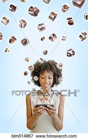 Stock Photo - African American woman using cell phone with images floating above. Fotosearch