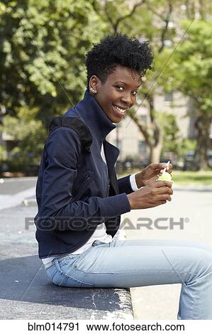 Stock Image - Black woman eating ice cream in park. Fotosearch