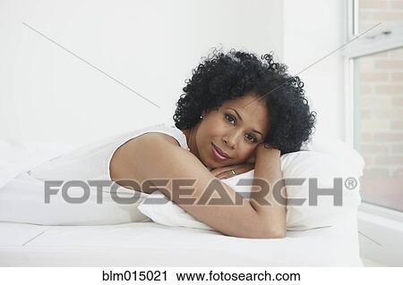 Stock Image - Black woman laying in bed. Fotosearch
