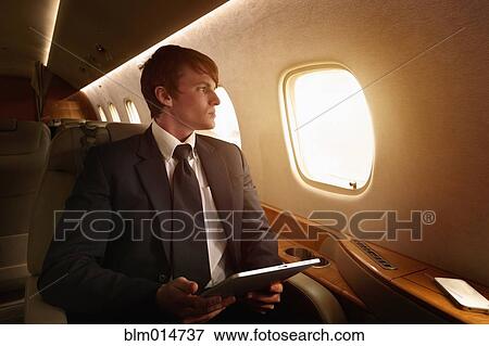 Stock Photo - Caucasian businessman using digital tablet on private jet. Fotosearch