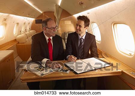 Stock Image - Caucasian businessmen working on private jet. Fotosearch