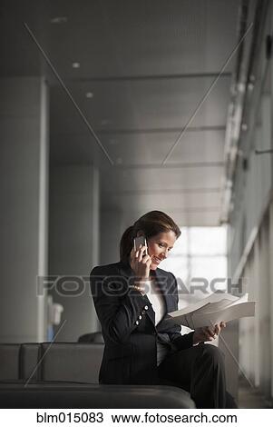 Stock Image - Caucasian businesswoman holding paperwork and talking on cell phone. Fotosearch