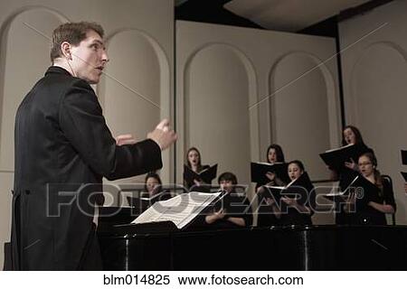Stock Photography - Caucasian conductor leading choir on stage. Fotosearch