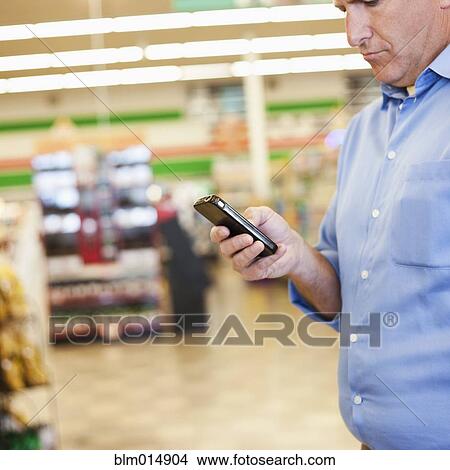 Picture - Caucasian man using cell phone in grocery store. Fotosearch