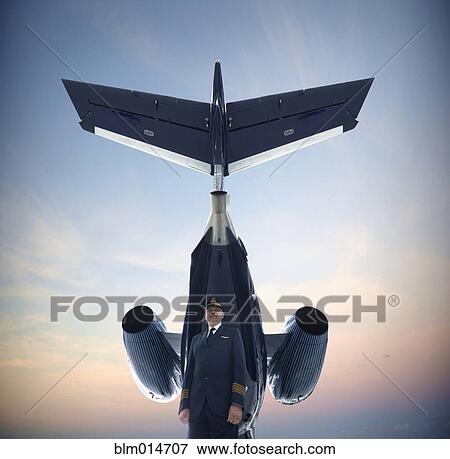 Stock Photo - Caucasian pilot standing underneath airplane. Fotosearch