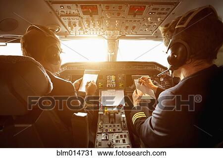 Stock Image - Caucasian pilots flying jet at sunset. Fotosearch