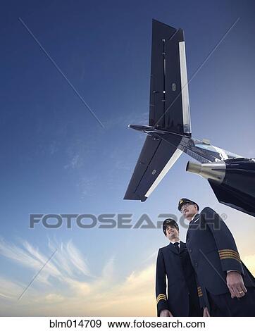 Stock Photo - Caucasian pilots standing underneath airplane. Fotosearch