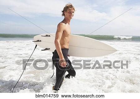 Stock Photo - Caucasian surfer carrying surfboard. Fotosearch