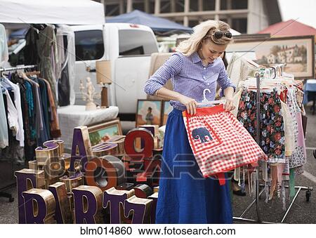 Stock Image - Caucasian woman shopping for apron in flea market. Fotosearch