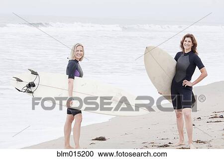 Stock Image - Caucasian women carrying surfboards. Fotosearch