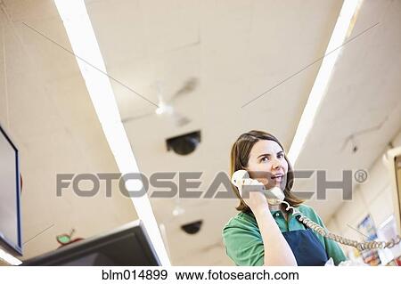 Caucasian worker talking on phone in grocery store View Large Photo Image Stock Photo - Caucasian worker talking on phone in grocery store. Fotosearch