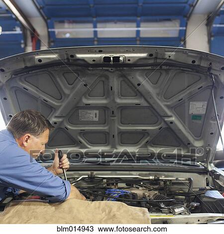 Stock Image - Caucasian worker working on automobile engine. Fotosearch