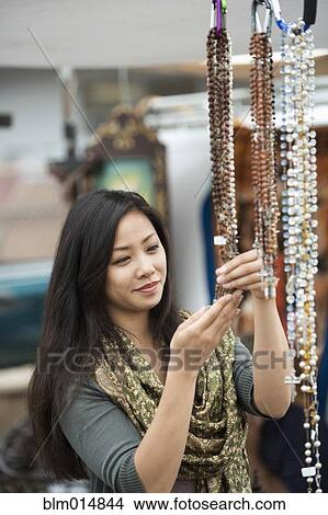 Picture - Chinese woman looking at jewelry in flea market. Fotosearch