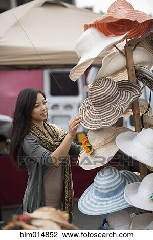 Stock Image - Chinese woman shopping for hats at flea market. Fotosearch