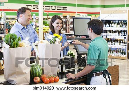 Stock Image - Customer paying cashier in grocer store. Fotosearch