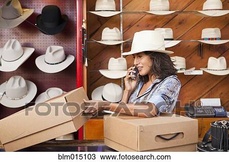 Stock Image - Ecuadorian woman talking on cell phone in hat store. Fotosearch