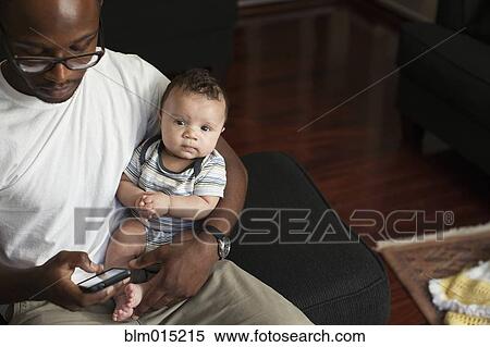 Stock Photography - Father holding baby and text messaging on cell phone. Fotosearch