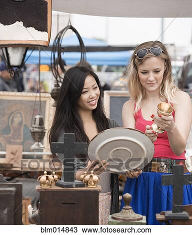 Stock Image - Friends looking at items in flea market. Fotosearch