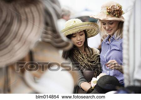 Picture - Friends shopping for hats at flea market. Fotosearch