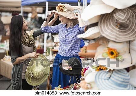 Stock Image - Friends shopping for hats at flea market. Fotosearch