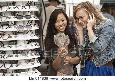 Stock Photo - Friends trying on glasses in flea market. Fotosearch