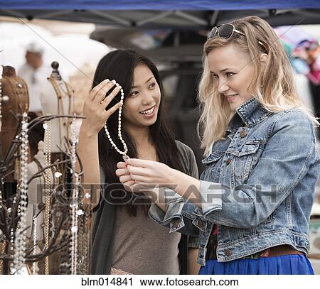 Stock Image - Friends trying on jewelry at flea market. Fotosearch