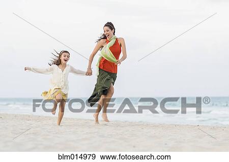 Stock Photo - Hispanic mother and daughter running on beach. Fotosearch