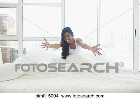 Picture - Hispanic woman in bed with arms outstretched. Fotosearch