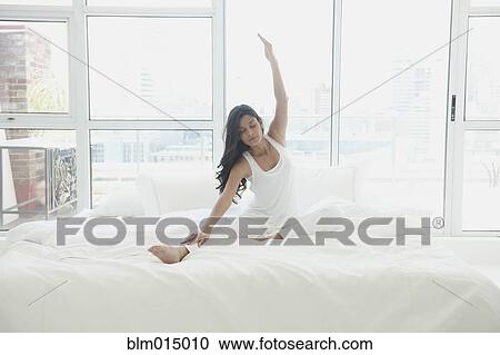 Stock Image - Hispanic woman in bed with arms outstretched. Fotosearch
