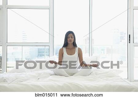 Stock Image - Hispanic woman meditating in bed. Fotosearch