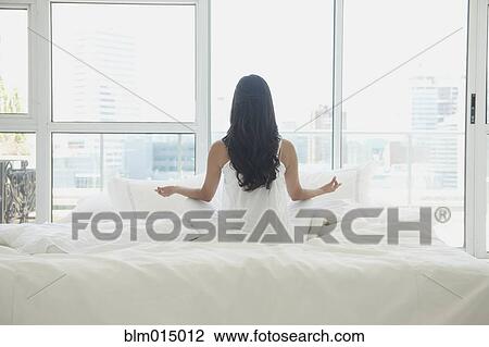 Stock Image - Hispanic woman meditating in bed. Fotosearch
